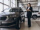 Female automotive manager at car dealership reviewing car specs on phone.